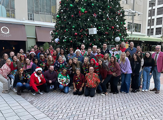 People smiling in front of a Christmas holiday tree.